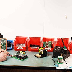 Bild von einem Arbeitsplatz in der Elektromontage. Mehrere Kästen mit Bauteilen sowie Werkzeuge.