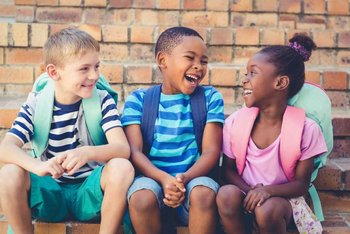 Drei fröhliche Schulkinder mit Rucksäcken sitzen auf einer Treppe aus Backstein und lachen miteinander. - Bild vergrößern Drei fröhliche Schulkinder mit Rucksäcken sitzen auf einer Treppe aus Backstein und lachen miteinander.