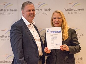 Zwei Personen lachen glücklich mit Urkunde in der Hand in die Kamera.