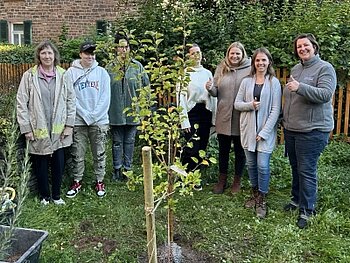 Kolleginnen und Klient:innen aus der Büdinger Tagesgruppe vor dem frisch gepflanzten Bäumchen.
