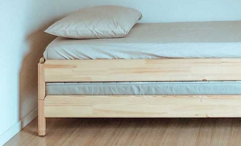 Einfach eingerichtetes Zimmer mit Holzbett und kleinem Tisch neben dem Bett.