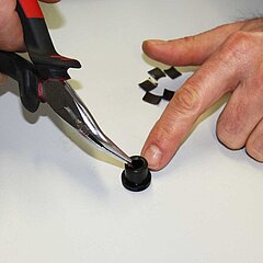 Bild aus dem Arbeitsbereich Montage. Man sieht eine Hand mit Zange und Kunststoffteil.