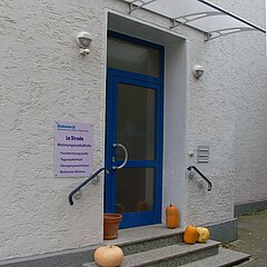 Eingangstür mit Schild: "La Strada, Wohnungsnotfallhilfe: Fachberatungsstelle, Tagesaufenthalt, Übergangswohnheim, Betreutes Wohnen"
