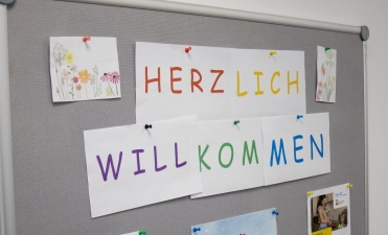Auf einer Tafel kleben Zettel mit bunten Buchstaben: Herzlich willkommen