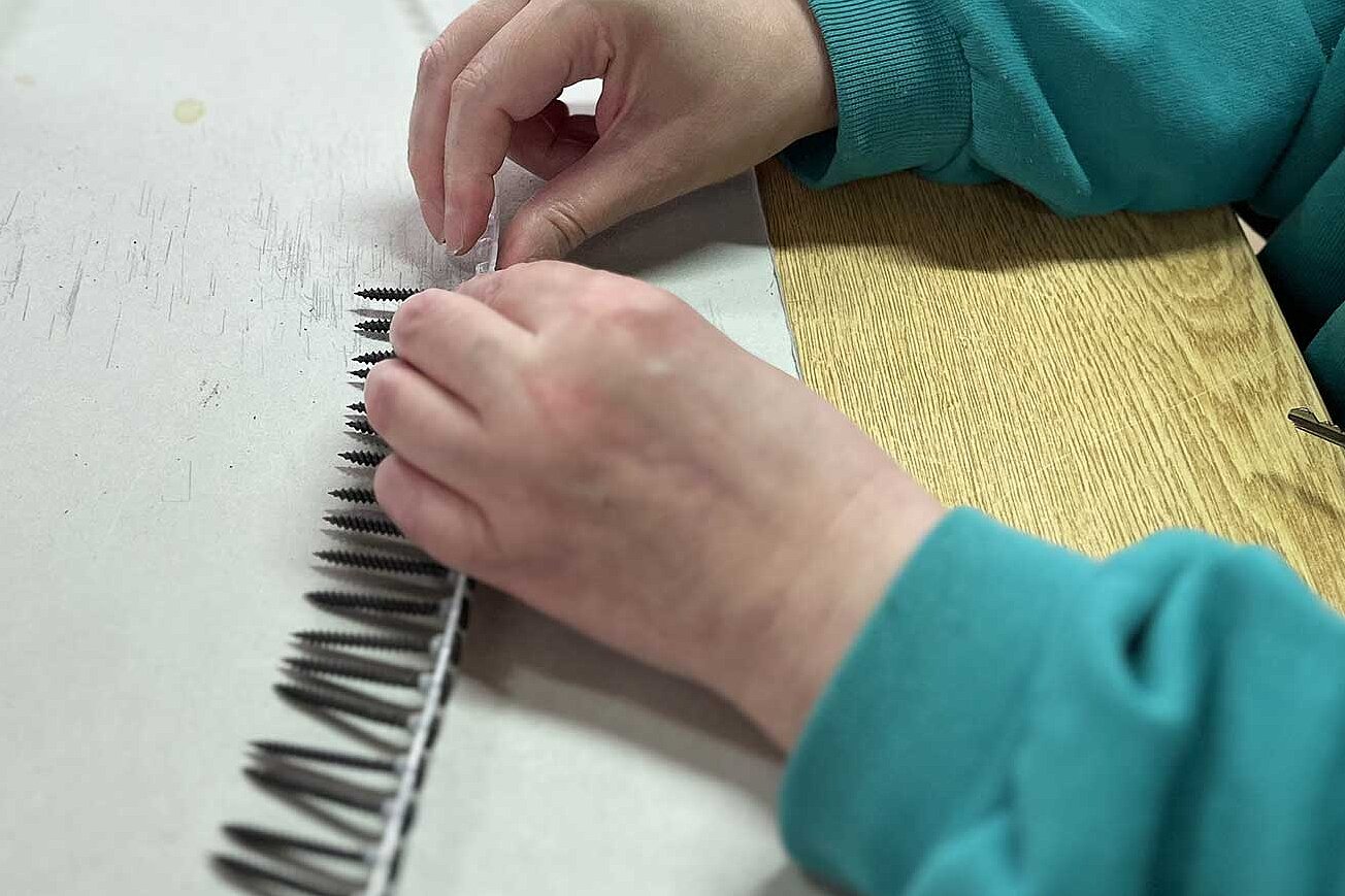 Bild von den Händen einer Person, die Schrauben und Kunststoffteile zusammenfügt.