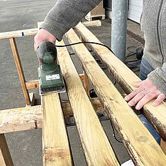 Bild vom Schleifen alter Balken, die auf Böcken liegen.